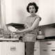 Black and white vintage photo of a woman unloading plates from a dishwasher with amazed expression